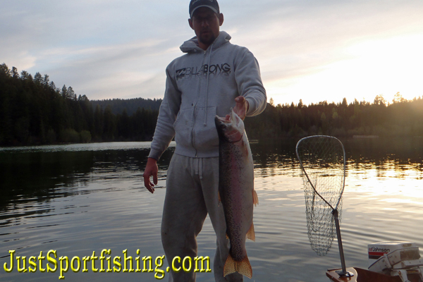 Fisherman standing on a dock holding a big rainbow trout.