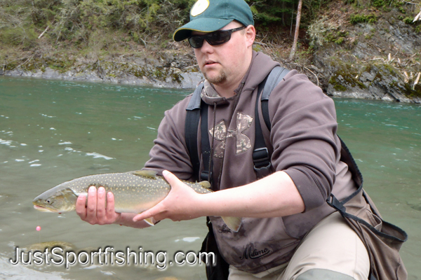 Fisherman holding a bull trout beside a river.