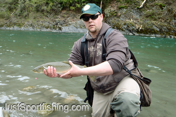 Fisherman holding a bull trout beside a river.