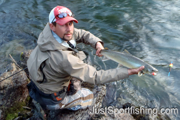 Photo of a fisherman by a river holding a dolly varden trout.