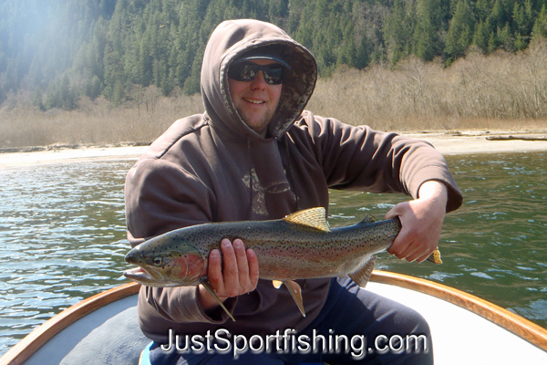 Fisherman holding a big rainbow trout in a boat.