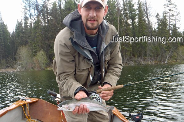 Fisherman on lake holding a small rainbow trout.