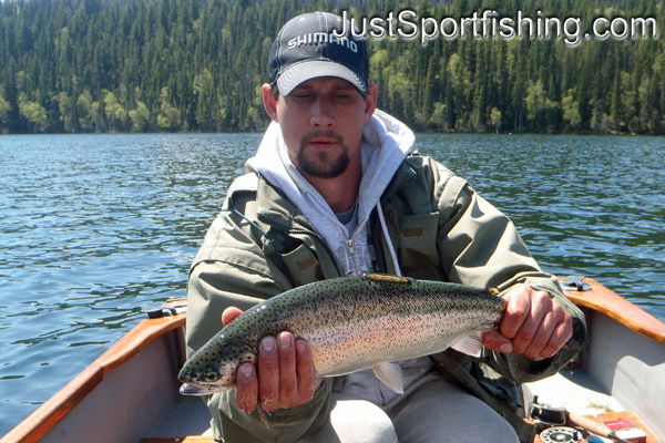 Fisherman in boat holding a rainbow trout.