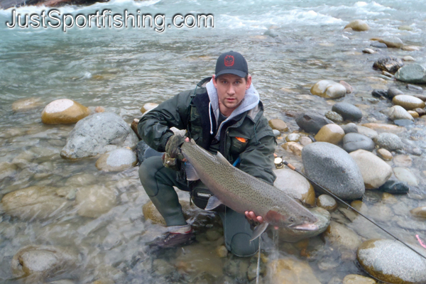 Fisherman holding a steelhead beside river.