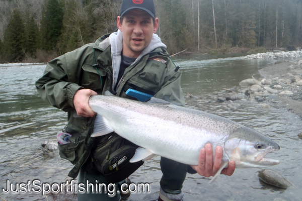 Fisherman kneeling with his steelhead trout in a river.