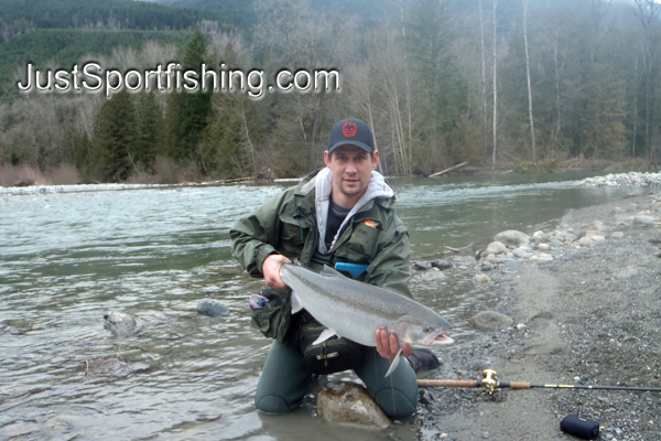 Fisherman kneeling at the rivers edge with a steelhead trout.