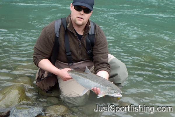 Fisherman kneeling at the rivers edge with a steelhead trout.