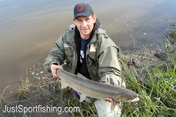 Fisherman kneeling at the rivers edge with a steelhead trout.