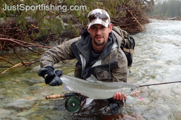 Fisherman kneeling at the rivers edge with a steelhead trout.