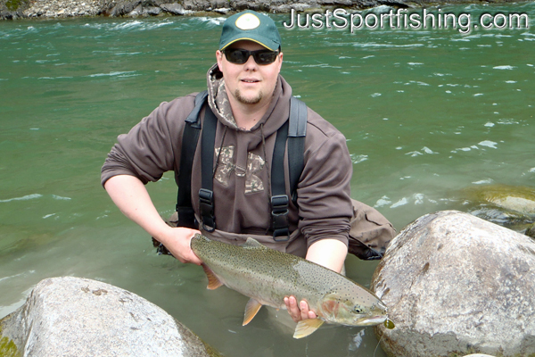 Fisherman holding a steelhead trout beside a river.