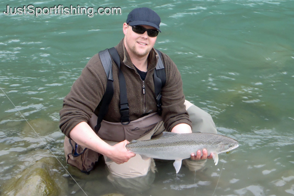 Fisherman kneeling in a river holding a big steelhead trout.